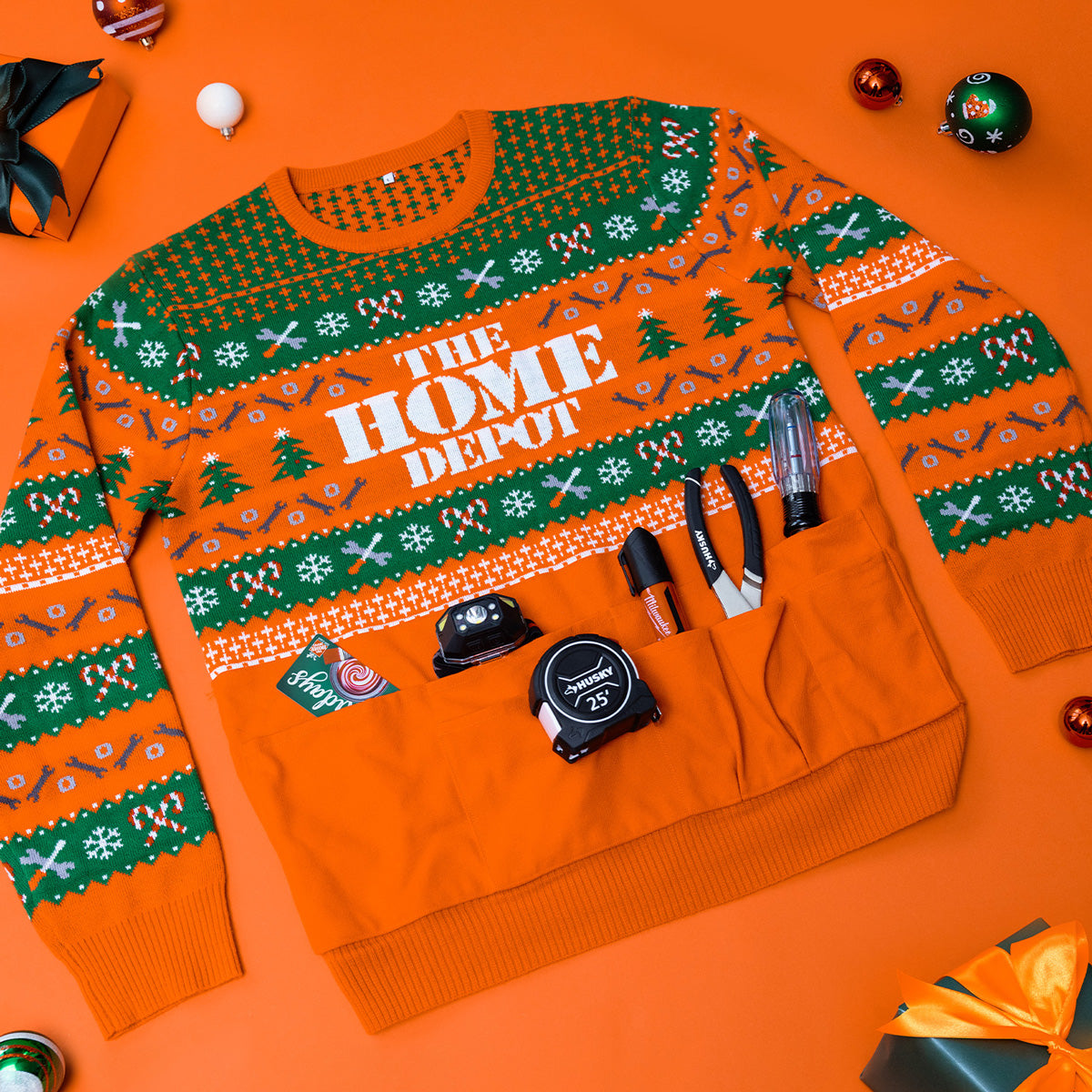 The Home Depot doer holiday sweater laid out with tools in the pockets of the front of the sweater.